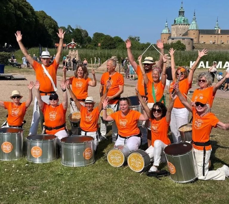 Strandskulpturfestivalen 2025 Batucalma poserar framför strandskulpturer med Kalmar slott i bakgrunden.